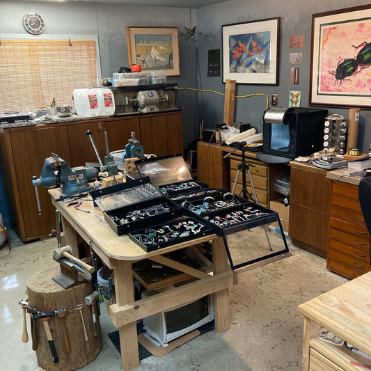 View of my studio with metal forming tools, and finished jewelry. Paintings hang on the walls, and chaos abounds.