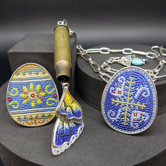 two pysanky micro-mosaic brooches and a bullet casing necklace with butterfly wings emerging as if from a chrysalis.