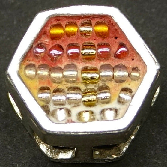 Hexagonal bead with orange and pink tones in an ombre pattern on a dark background